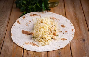 Tortiliją pašildykite sausoje keptuvėje, kad suminkštėtų ir nelūžtų vyniojant. Į centrą dėkite 1/4 viso įdaro ir pabarstykite tarkuotu sū...