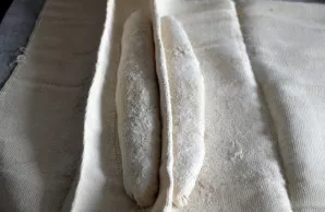 Perkelkite bagetų ruošinius ant miltais pabarstytos drobės siūle žemyn. Padarykite pertvarą tarp ruošinių. Uždenkite plėvele ir palikite ...