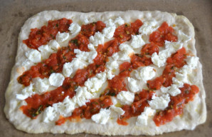 Ant tešlos lakšto sudėkite gabalėliais suplėšytą mocarelą ir pomidorų padažą su baziliku, kaip ruošiant picą „Margarita“.