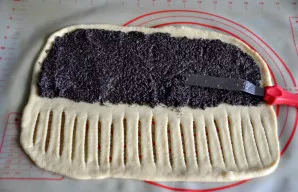 Ant pusės tešlos lakšto užtepkite aguonų įdarą ir išlyginkite. Kitą laisvą pusę supjaustykite ~1 cm pločio juostelėmis, palikdami 5–6 cm ...