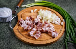 Per tą laiką paruoškite padažą. Šoninę supjaustykite mažais gabaliukais, o antrą svogūną smulkiai supjaustykite.