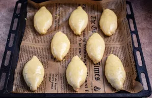 Paruoštus pyragėlius dėkite ant kepimo popieriumi išklotos skardos siūle žemyn. Kiekvieną aptepkite išplakto kiaušinio trynio ir 1 arbat....