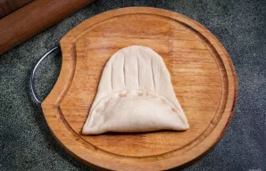 Užlenkite tešlą ant kremo ir užspauskite kraštus. Laisvoje dalyje padarykite įpjovas.