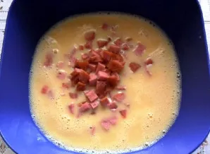 Tada supjaustykite dešrelę mažais gabalėliais ir sudėkite į kiaušinių masę.