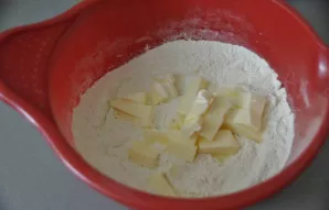 Sudėkite gabalėliais supjaustytą atšaldytą sviestą ir įtrinkite jį su miltais iki trupinių.