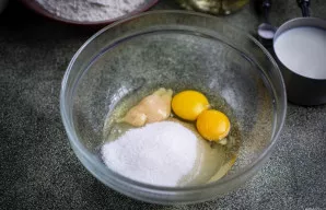 Į dubenį su dviem tryniais suberkite cukrų ir įdėkite medų.