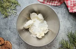 Kreminį sūrį sudėkite į dubenį, suberkite cukraus pudrą, vanilinį cukrų ir plakite 2 minutes iki purumo.