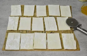 Sluoksniuotą tešlą iš anksto atitirpinkite šaldytuve. Išklokite ją ant kepimo popieriaus, lengvai pabarstyto kukurūzų krakmolu. Supjausty...