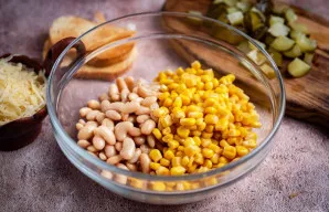 Į didelį dubenį sudėkite konservuotas pupeles ir konservuotus kukurūzus.