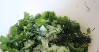 Į svogūną sudėkite susmulkintus žalumynus, krienus ir kubeliais pjaustytą agurką. Supilkite aliejų, įberkite druskos ir pipirų.