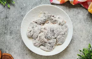 Dubenyje suberkite miltus ir sudėkite iš pieno išimtą jautienos kepenis, išmaišykite, kad kiekvienas gabaliukas apsiveltų.