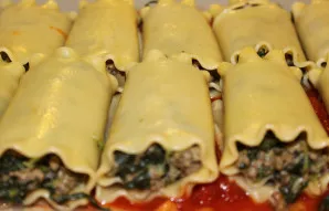 Į kepimui atsparios formos dugną įdėkite kelis šaukštus pomidorų padažo. Įdarykite kanelonus atvėsusiu įdaru ir dėkite į formą.