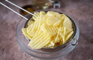 Tada naudodami kiaurasamtį nupilkite perteklinį skystį ir nusausinkite bulvių griežinėlius popieriniais rankšluosčiais.