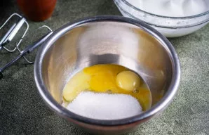 Į kitą dubenį sudėkite trynius ir įdėkite cukrų.