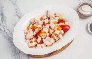 Rūkytą vištienos filė supjaustykite nedideliais kubeliais ir taip pat sudėkite į salotinę.