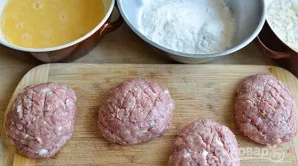 Ant kotletų padarykite įpjovas. Apvoliokite mėsos gaminius plaktame kiaušinyje, o po to - miltuose.