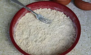 Viską sumaišykite šakute ir ant dugno paskleiskite trupininės tešlos sluoksnį, šiek tiek prispausdami.