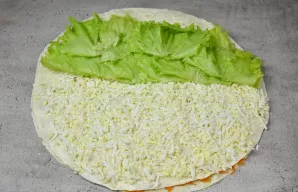 Ant viršaus uždėkite trečią lavašą. Patepkite jį likusiu padažu. Ant vienos pusės išdėliokite sluoksnį virtų, tarkuotų kiaušinių ir galia...