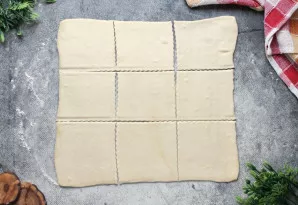 Lengvai pabarstykite stalą miltais, dėkite tešlą ir šiek tiek iškočiokite, geriausia - kvadrato formos. Supjaustykite į devynias dalis. P...