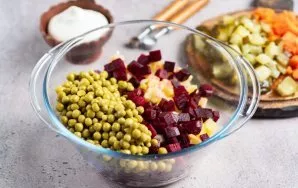 Į didelį salotų dubenį sudėkite kubeliais pjaustytas bulves ir burokėlius, suberkite konservuotus žirnelius.