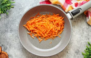 Kol verda daržovės, paruoškite apkepą ščiams. Tam morką sutarkuokite stambia tarka ir sudėkite į keptuvę su augaliniu aliejumi.