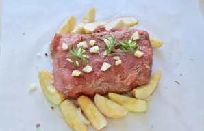 Obuolius išdėliokite aplink mėsą. Ant viršaus uždėkite supjaustytą česnaką ir rozmarino šakeles.