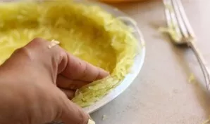 Šakute iškastą moliūgo minkštimą sudėkite į riebalais pateptą kepimo indą. Prispauskite ir suformuokite kraštelius.
