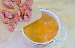 Paruoštą daržovių apkepą sudėkite į puodą su sriuba. Įdėkite griežinėliais pjaustytas medžiotojų dešreles.