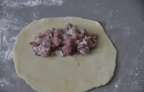 Pabarstykite stalą miltais, iškočiokite tešlą į paplotėlį, ant vieno krašto dėkite mėsos įdarą.