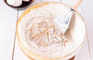 Perkelkite paruoštą tešlą iš puodynės į didelį indą ir įmaišykite likusius miltus.