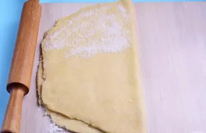 Tešlą perlenkite ir ant pusės sulenktos tešlos vėl suberkite dalį cukraus.