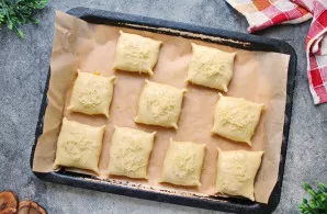 Kepimo skardą išklokite kepimo popieriumi ir išdėliokite pyragėlius siūle žemyn, palikdami nedidelius tarpus. Sumaišykite trynį su vanden...