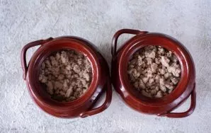 Ant bulvių sluoksnio puoduose sudėkite keptą faršą. Į kiekvieną puodą įpilkite 50 ml vandens ir suberkite pipirus.