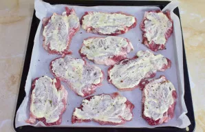 Kepimo skardą išklokite kepimo popieriumi ir sudėkite išmuštą mėsą. Aptepkite ją majonezu. Pabarstykite prieskoniais.