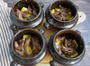 Į puodelių dugną sudėkite bulves, ant viršaus - apkepintą mėsą.